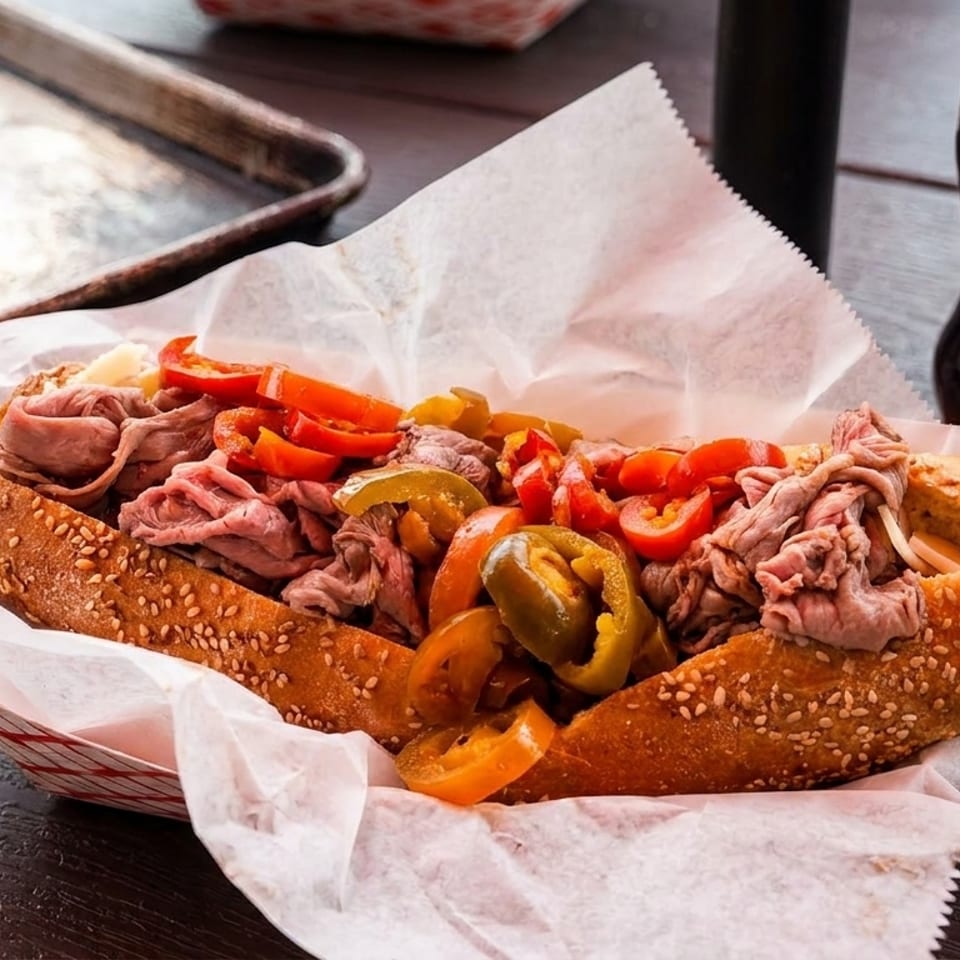 A large Italian beef sandwich with peppers and an A&W root beer on a wooden table.